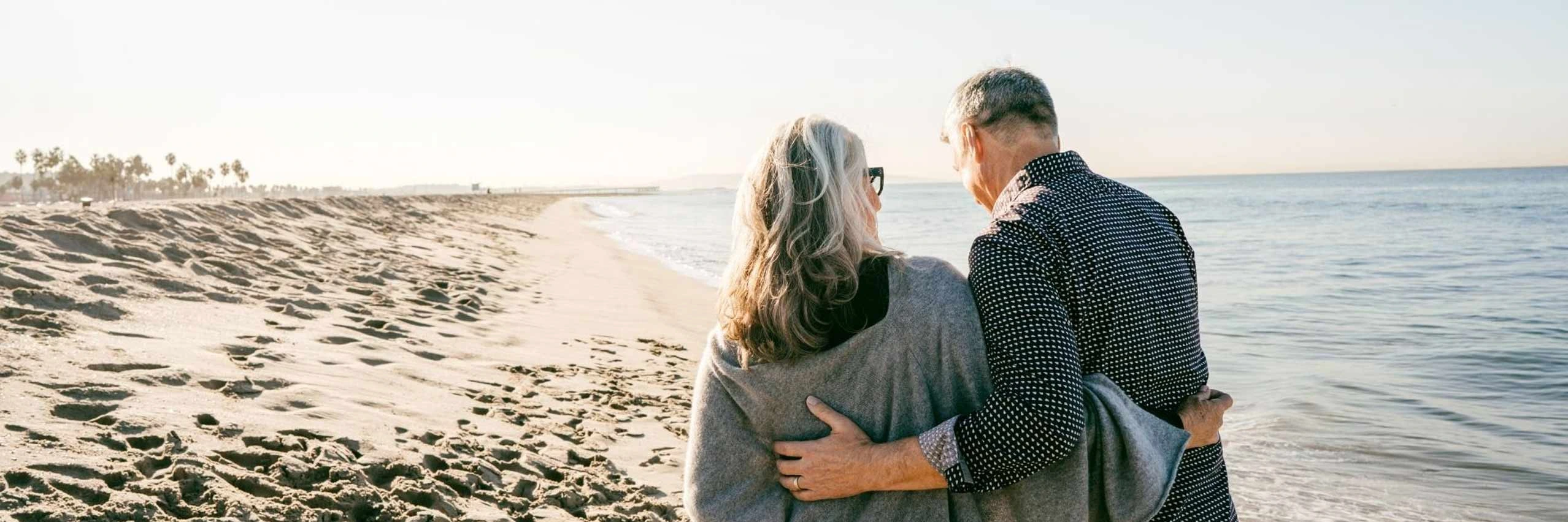 Una pareja mayor caminando por la playa, tranquilos y felices al contar con un seguro de vida